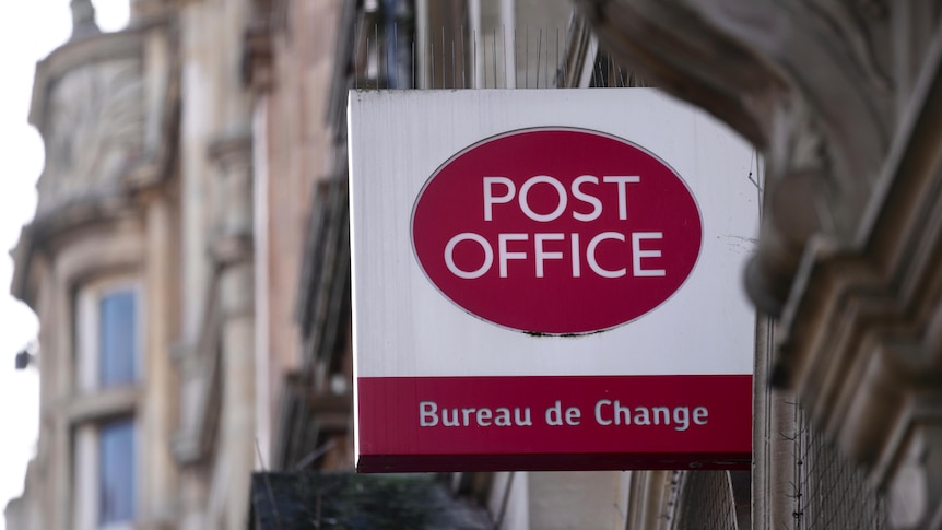 A red and white logo sticking out of a building which reads Post Office Bureau de Change.