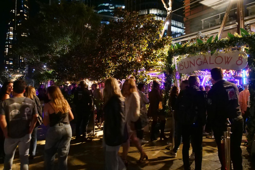 Crowds of people and a line up of people entering a nightclub. Sign says Bungalow.