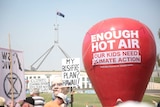 A large red balloon dominates the shot, with a banner on it saying "enough hot air", in front of Parliament House.