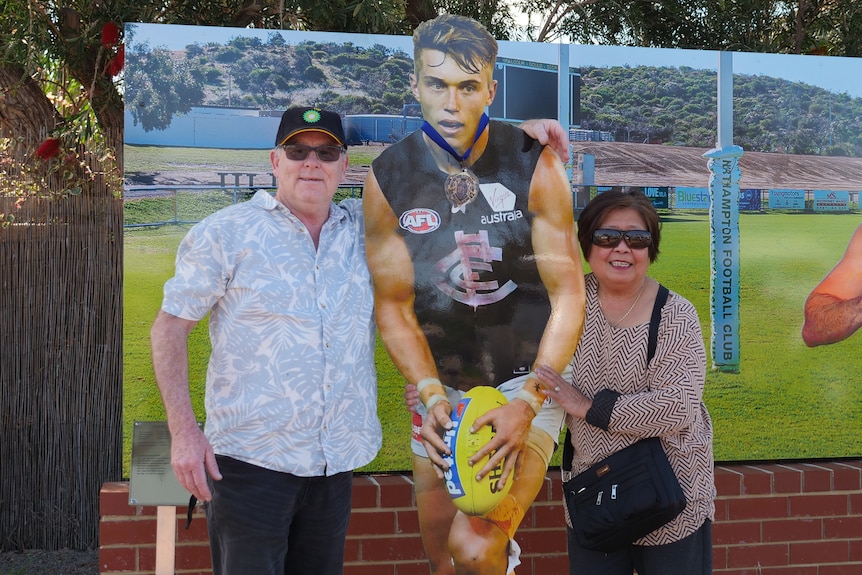 Two people pose for a photo next to statue of an AFL player.