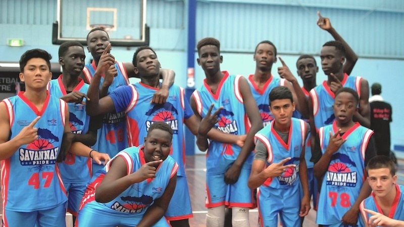 A group of teenagers post with "number one" symbol with their hands while wearing basketball uniforms