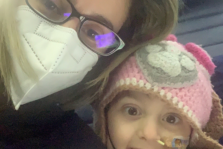 Kristy Colakidis wears a face mask on a plane while her young daughter smiles next to her.