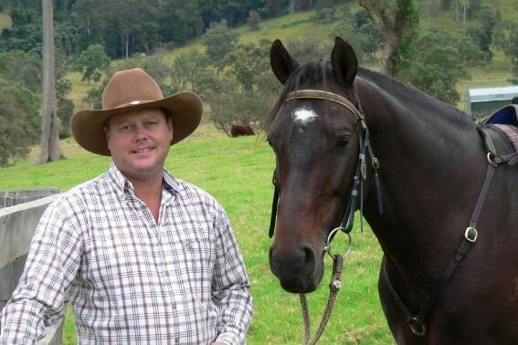 A man wearing a hat and a checked shirt stands beside a horse