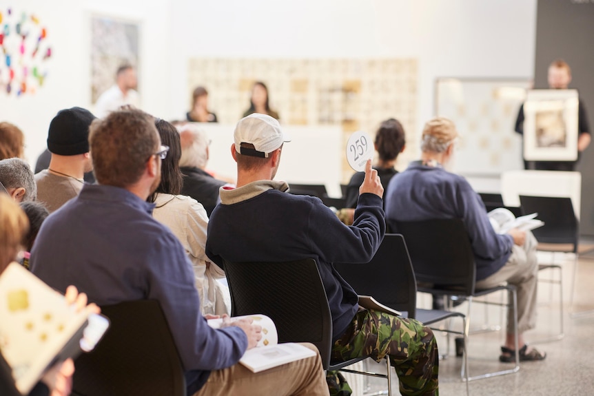 A man makes a bid for a piece of art at an auction.