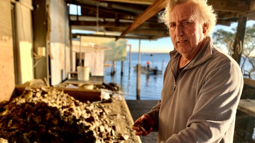 A man in a grey jumper stands at a table overflowing with oyster shells.