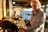 A man in a grey jumper stands at a table overflowing with oyster shells.