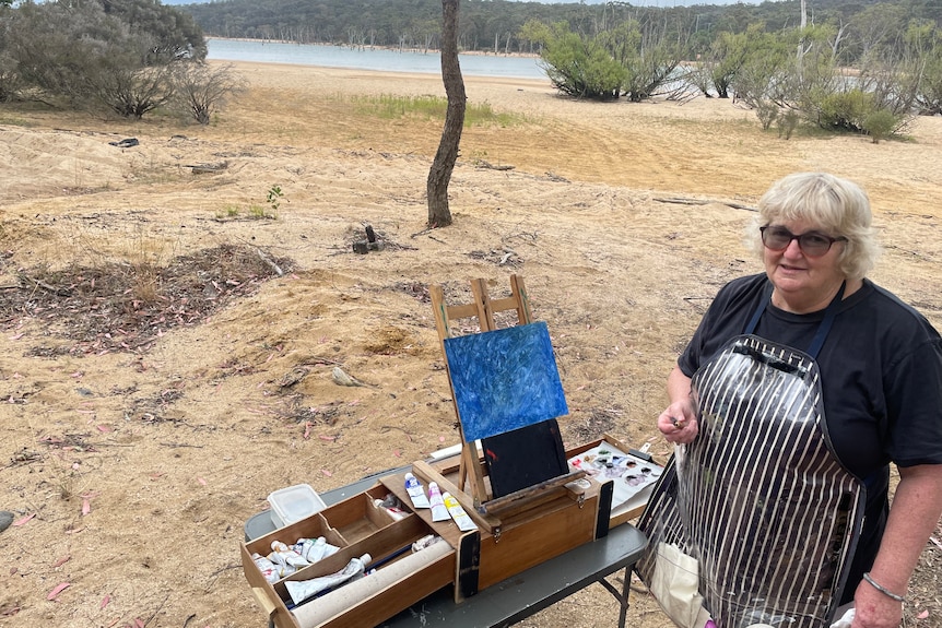 Dawn Stubbs standing with her painting at the lake