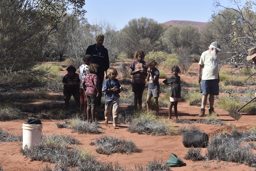 A group of children in the bush with three men supervising.