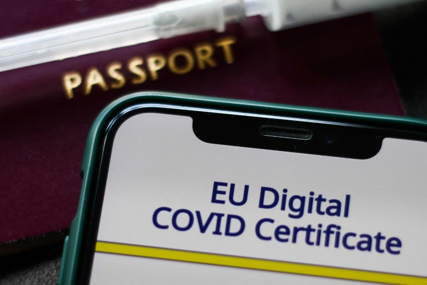 EU Digital COVID Certificate displayed on a phone screen, passport and medical syringe are seen.