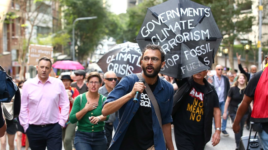 A man carrying a microphone marches in front of people carrying signs protesting climate change.