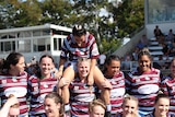 A group of women in rugby jerseys celebrate on a football pitch