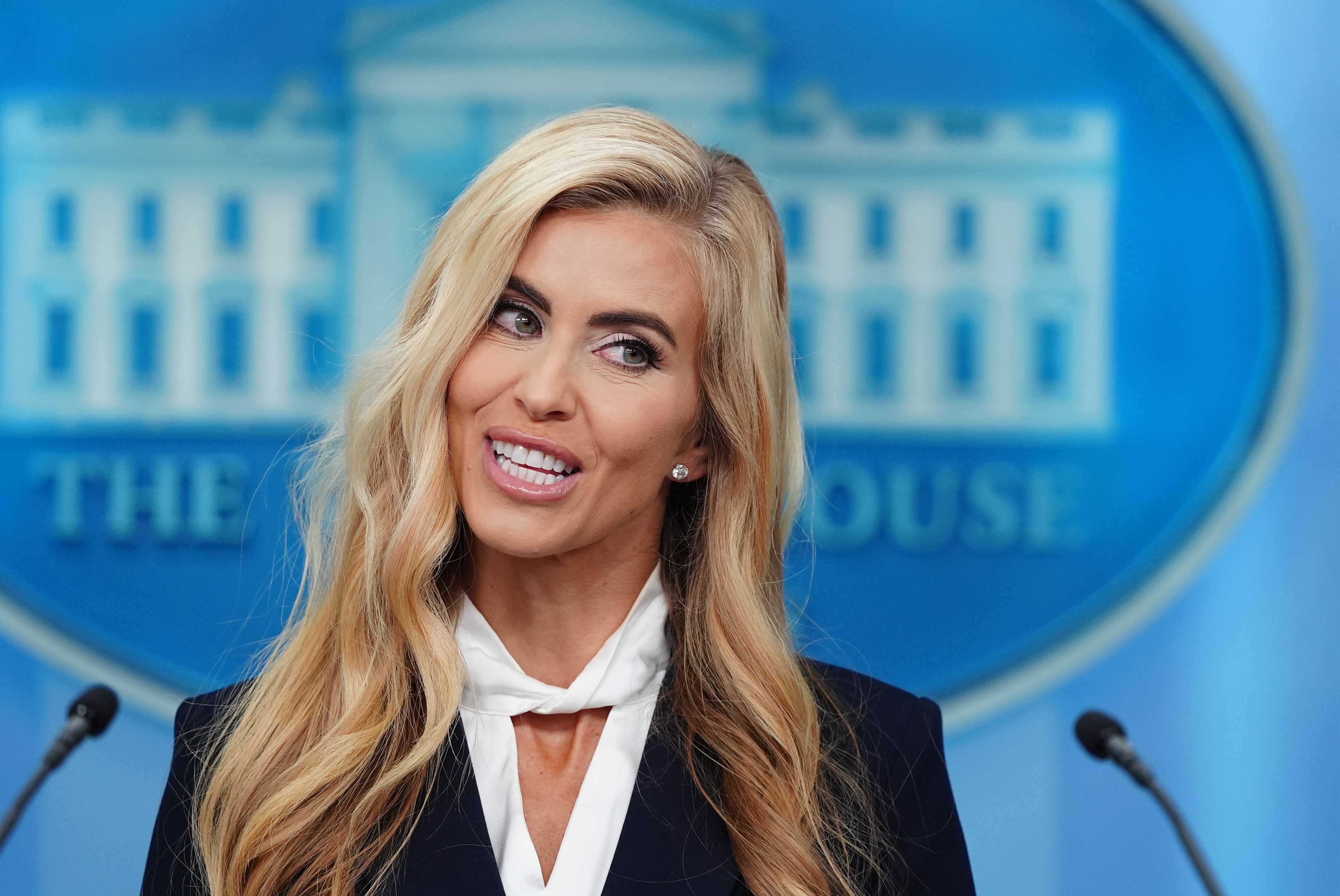 A woman with blonde hair speaking at a lectern in front of the White House emblem.