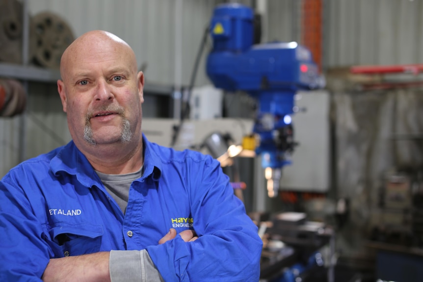 A man wearing a blue shirt crosses his arms inside a workshop