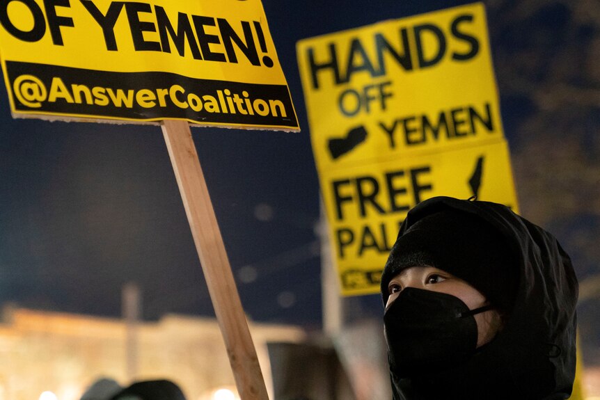 Woman wearing black mask holds up sign saying 'hands off yemen'.