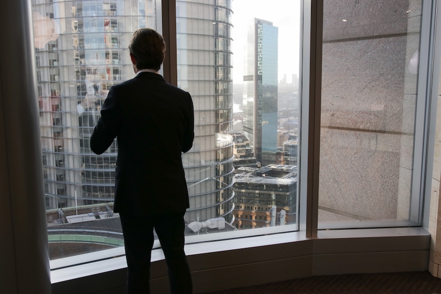 An unidentifiable man in suit in a high rise office, photographed from behind.
