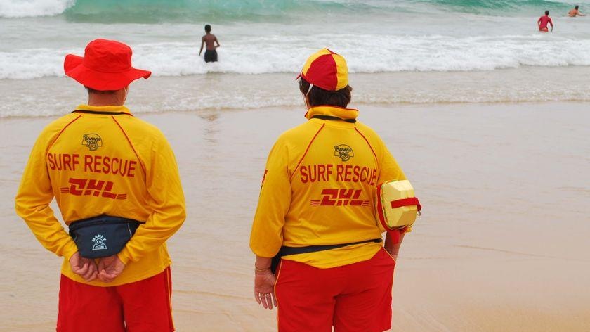 Two surf lifesavers standing on the beach. Photo taken from behind.