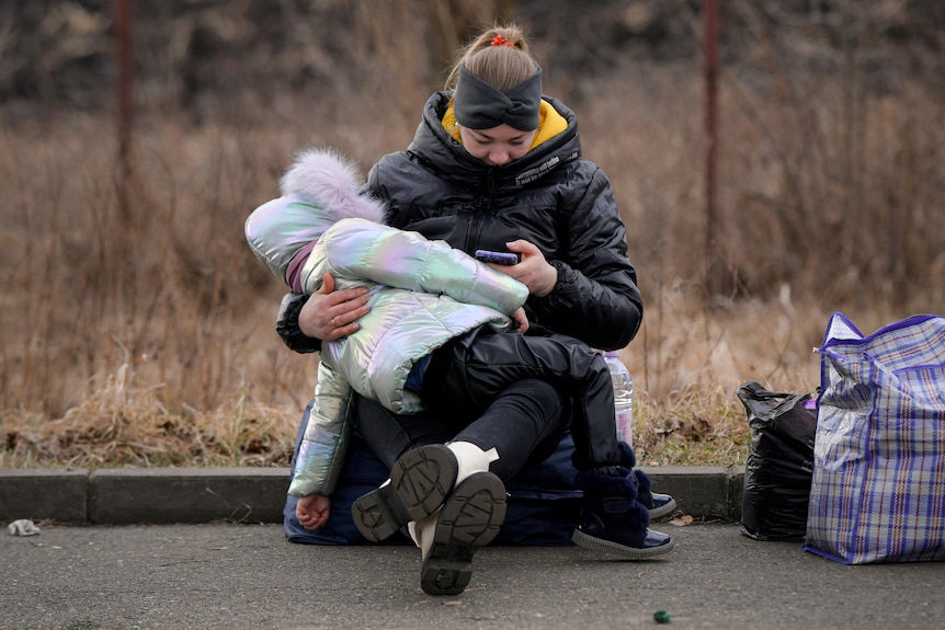 A woman nurses a child on the road. 