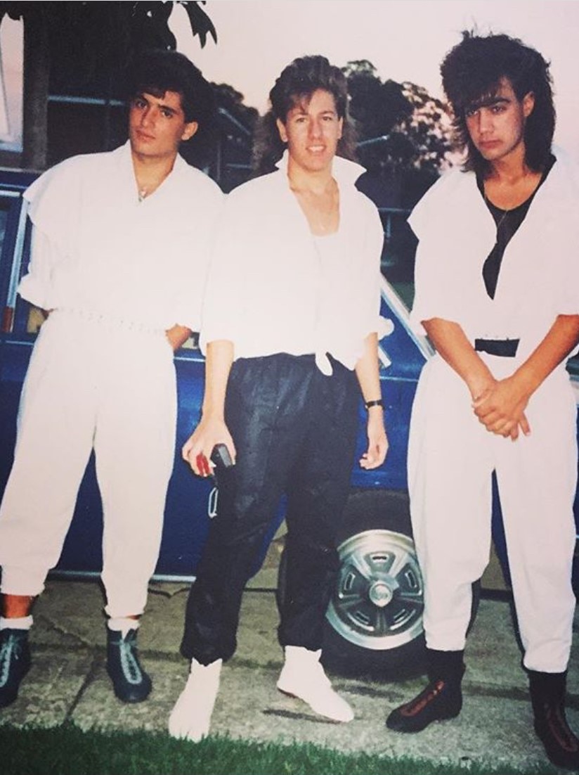 Retro photo of Arnie in his early twenties alongside two friends. They have big hair, boxing shoes, and popped collars.