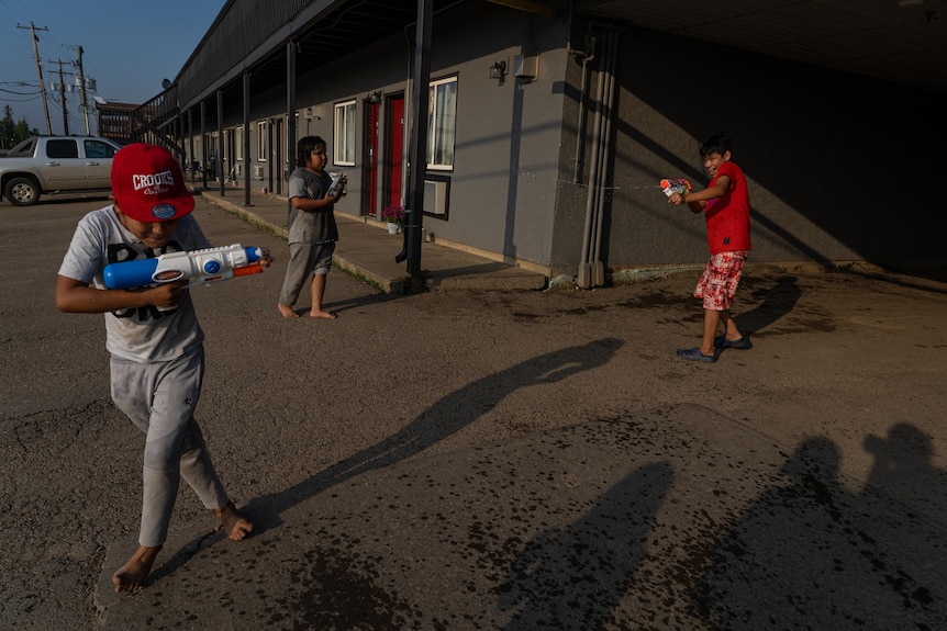 Three kids have a water fight with water guns on the concrete driveway of a motel in the afternoon sun.