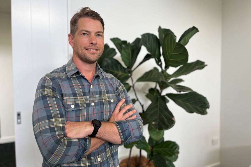 A man standing by a plant in his office with his arms crossed. 