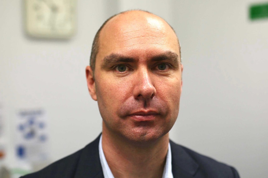 A headshot of Ben Scalley wearing a suit in a medical lab.