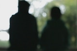 A silhouette of two people sitting on a bed with their backs towards the camera.