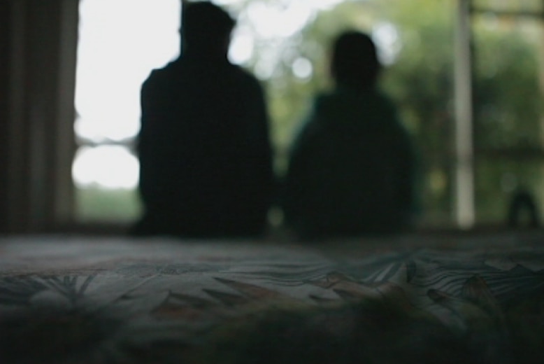 The silhouette of a child sitting on a bed with an adult sitting alongside them.