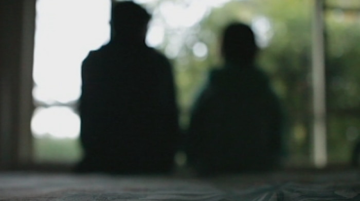 Silhouettes of a man and a child sitting on a bed indoors.