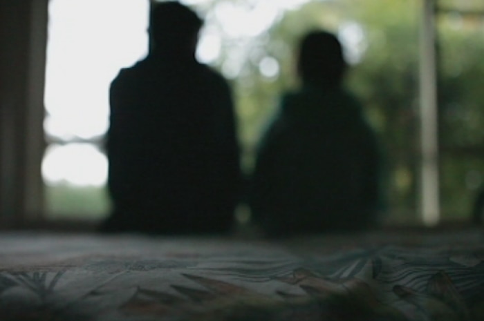The dark silhouette of a child sitting next to an adult.