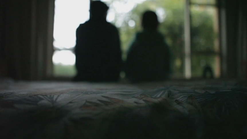 The silhouette of a child sitting on a bed with an adult sitting alongside them.