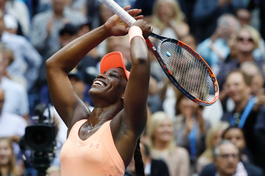 Tennis player smiles and holds her racquet above her head as she celebrates her victory.