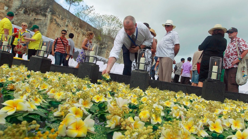 A man lays a flower into a pond for victims of the 2002 Bali bombings