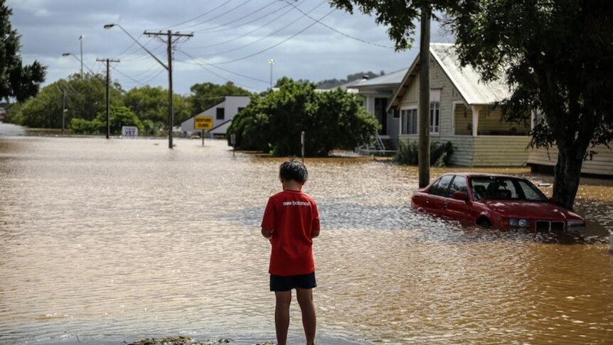 A kid stands in front of the floodwaters.
