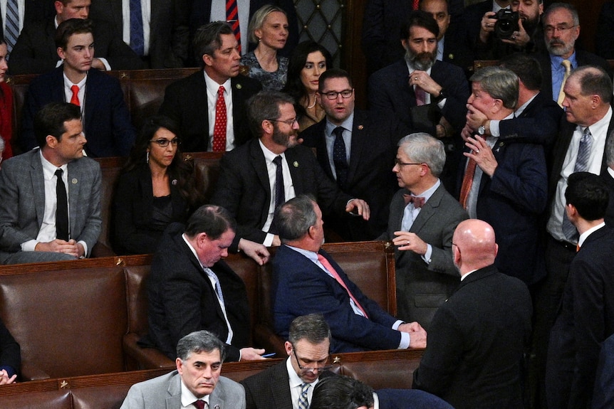 A man grabs another man around the mouth in a crowded room