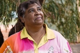 An indigenous woman with short hair wearing a pink shirt with a yellow collar