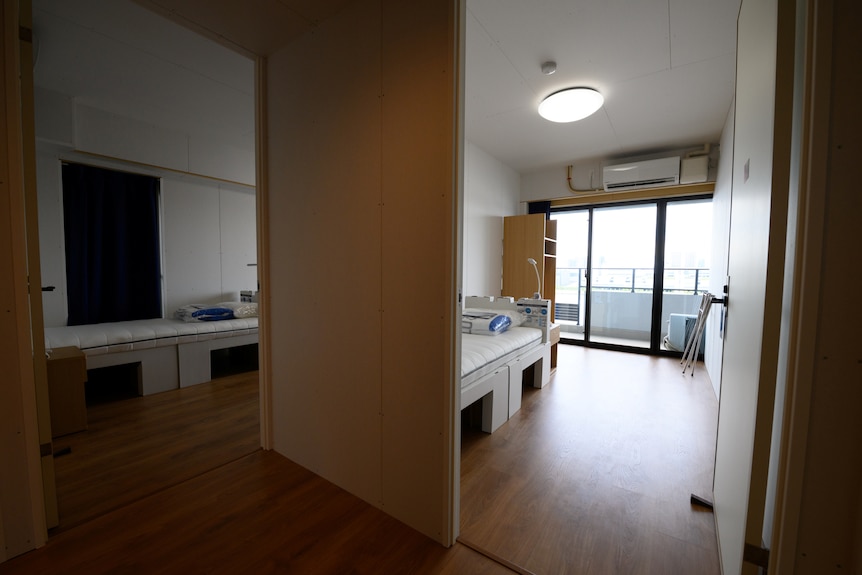 General view of bedrooms in a residential unit for athletes, showing single adjoining beds and minimal furniture