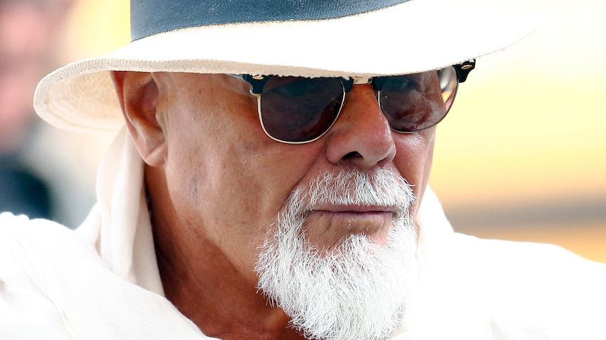 A man with a white goatee wearing sunglasses and a white hat.