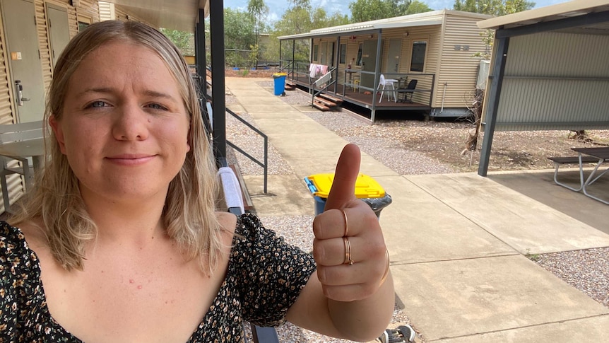 A woman with blonde hair stands in a quarantine facility near Darwin, giving a thumbs up.