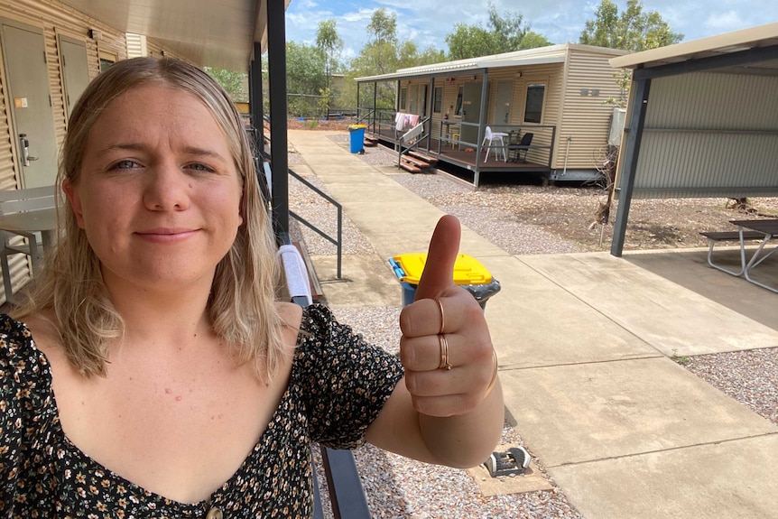 A woman with blonde hair stands in a quarantine facility near Darwin, giving a thumbs up.