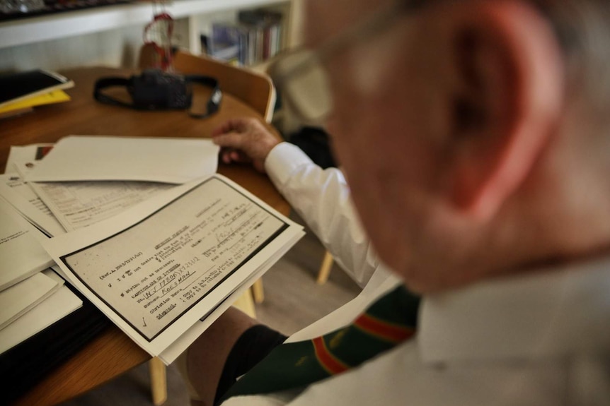 War veteran Matthew Rennie sits at a desk and examining a pile of papers.