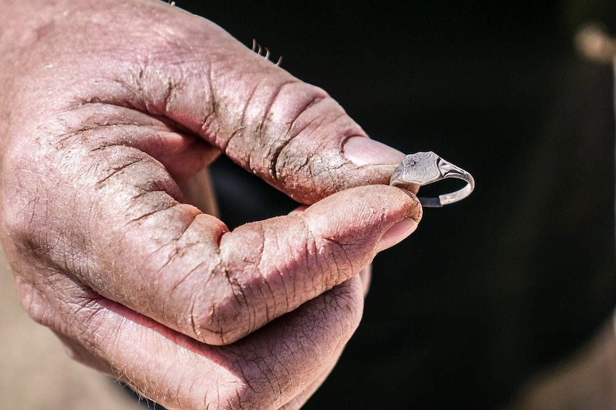 A close-up of a man's hand holding a small signet ring.