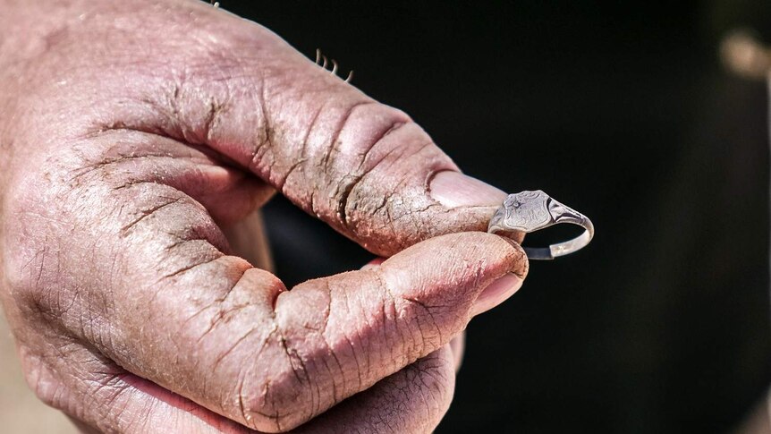 A close-up of a man's hand holding a small signet ring.