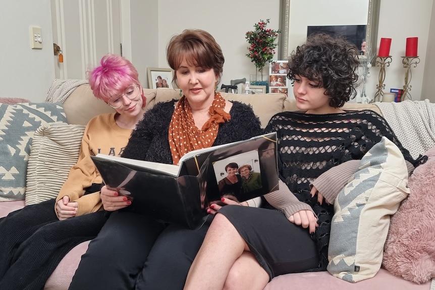 Mother sitting between her two daughters on a couch, looking at a photo album.