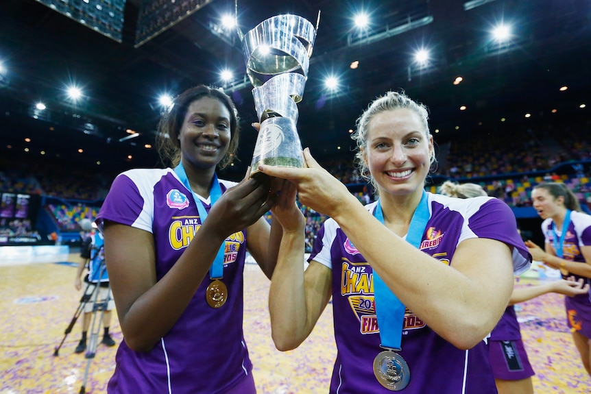Mid-shot of two Firebirds players, Romelda Aiken-George and Laura Geitz holding the ANZ Championship Trophy aloft.