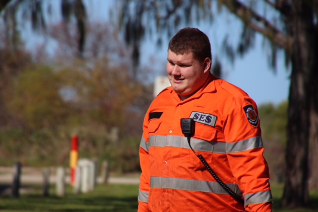 An SES volunteer wearing a bright orange hi-vis jacket walks outdoors.