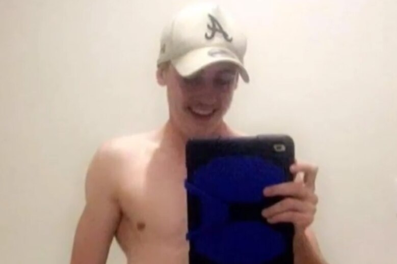 Ethan McPherson taking a photo of himself in a mirror with a tablet. He is shirtless and wearing a white Atlanta Braves hat.