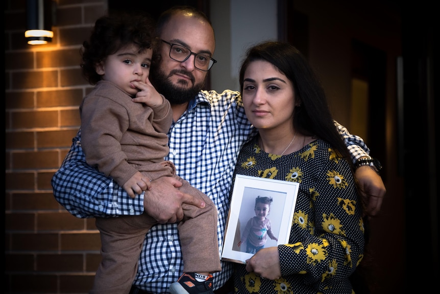 a family of three holding a portrait of a woman