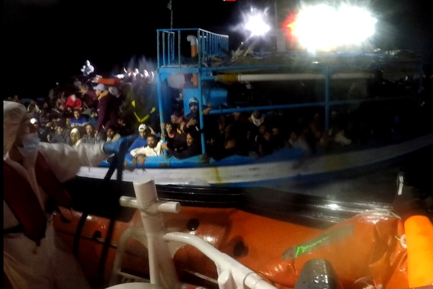 Italian coastguard members throw a rope to a boat in distress carrying migrants.