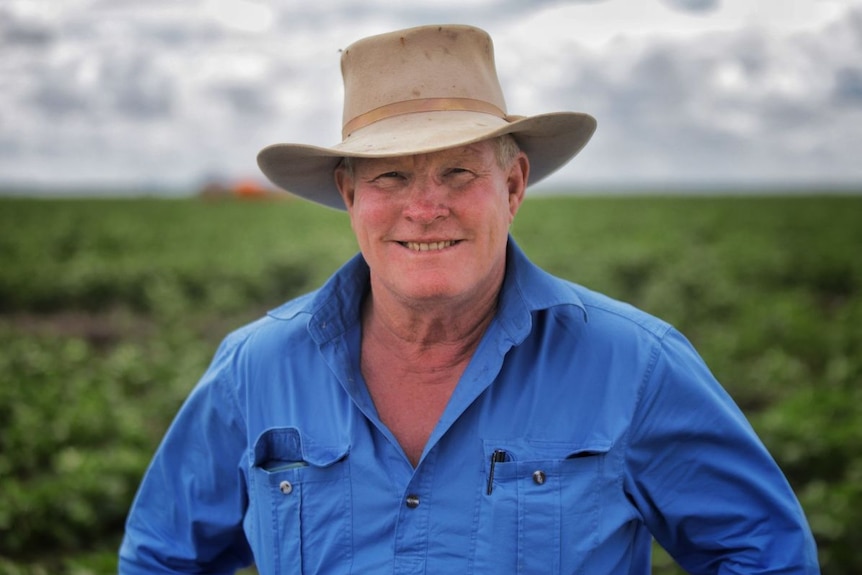 A man in a blue shirt and a hat smiles.