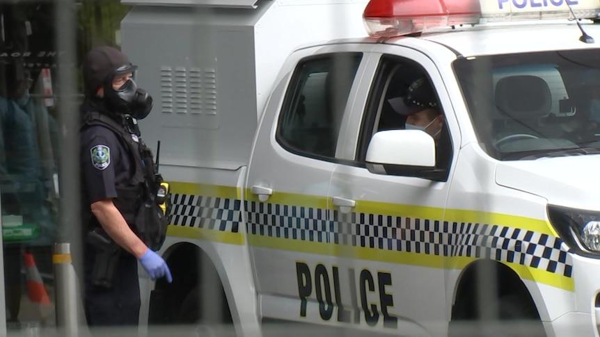 A police officer wearing a gas mask points at another police officer in the front seat of a wagon